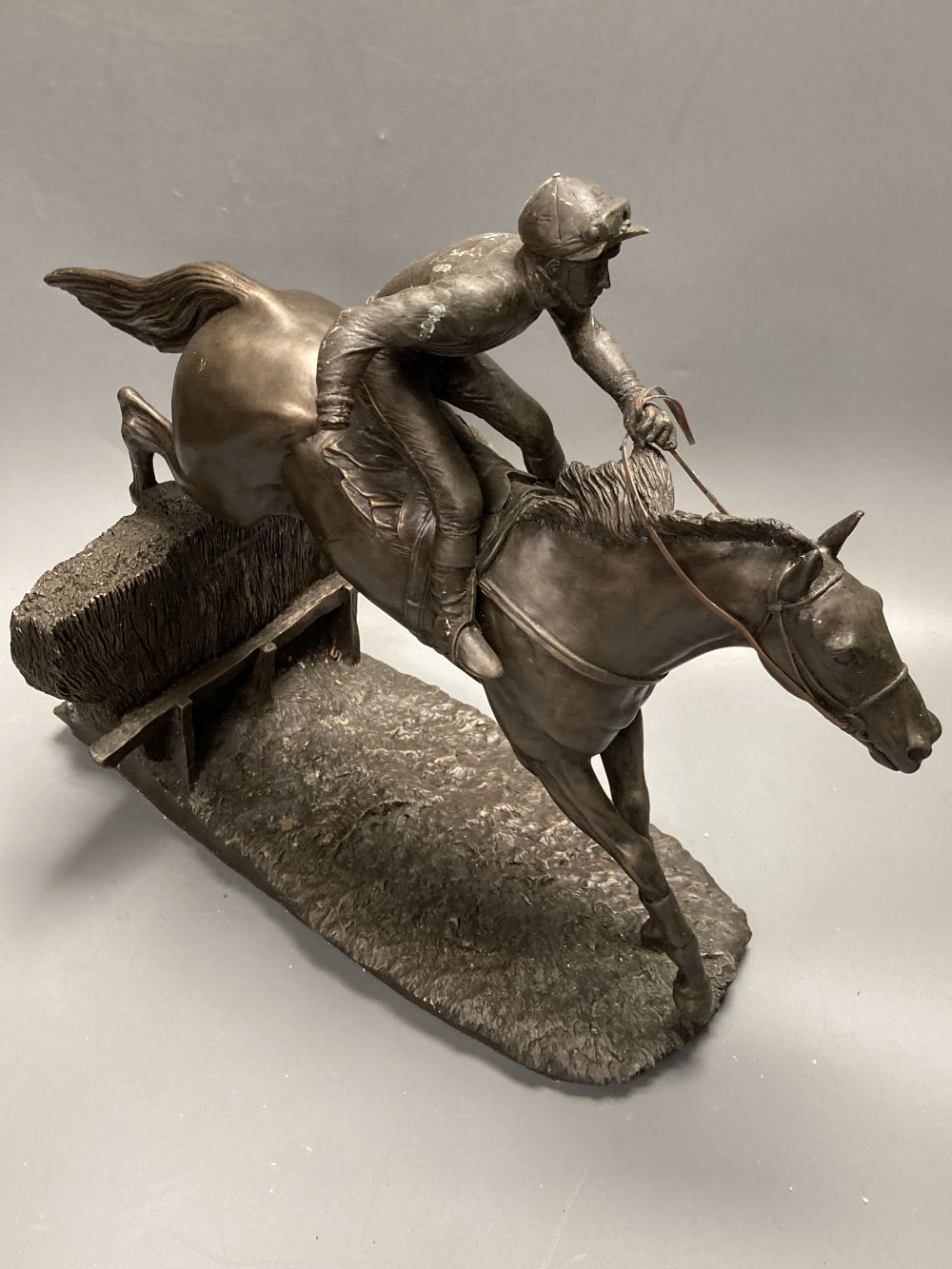 Two bronzed resin models of a steeplechasers, taking a fence, widest 35cm